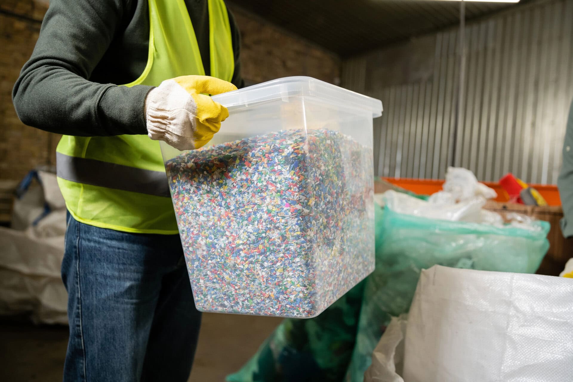 Cropped view of worker in high visibility vest and glove holding container with plastic for recycle while working in garbage sorting center, garbage sorting and recycling concept